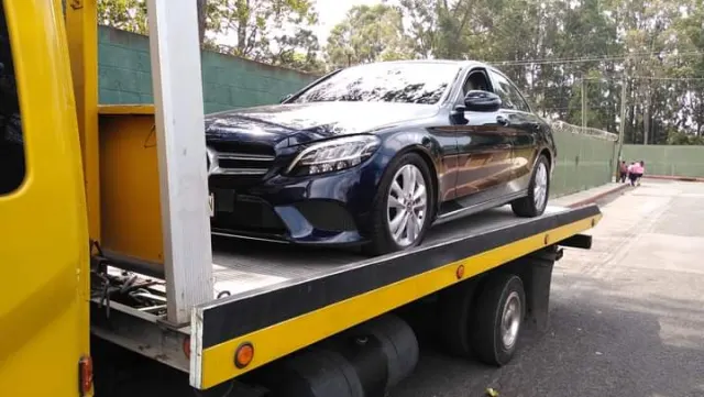 Grúa de plataforma amarilla transportando un automóvil negro