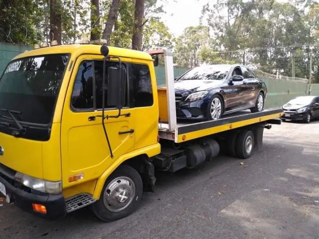 Grúa de plataforma amarilla transportando un automóvil negro